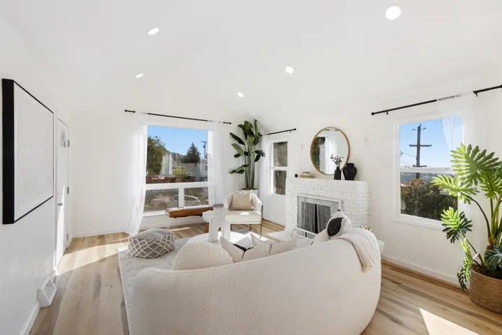 Living room featuring light wood-type flooring, plenty of natural light, a brick fireplace, lofted ceiling, and recessed lighting