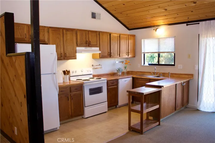 The living room & kitchen areas features an open and airy design, enhanced by a beautiful vaulted ceiling constructed with authentic tongue-and-groove wood paneling, creating a warm and inviting atmosphere.