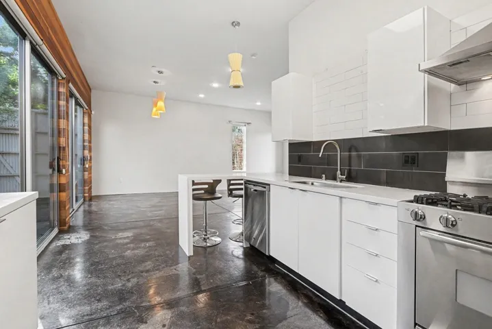 Kitchen with white cabinets, modern cabinets, range hood, concrete flooring, and stainless steel appliances