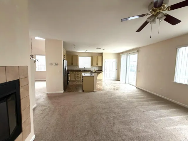 Unfurnished living room featuring a tiled fireplace, light colored carpet, and a ceiling fan