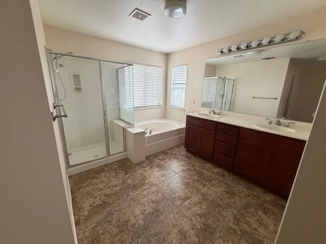 Bathroom with a stall shower, double vanity, a garden tub, a textured ceiling, and dark tile patterned flooring
