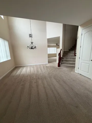 Unfurnished living room featuring stairs, carpet flooring, healthy amount of natural light, a high ceiling, and a chandelier