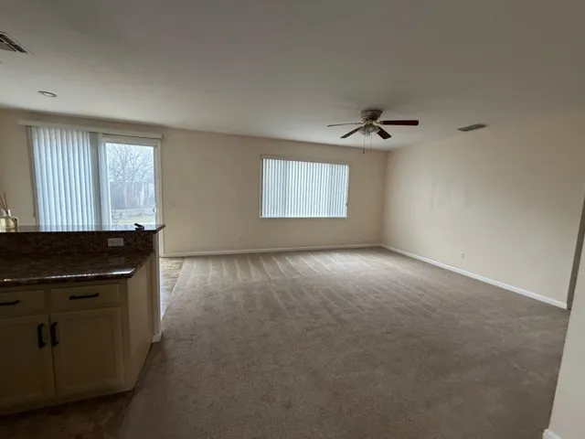 Unfurnished living room featuring light colored carpet, plenty of natural light, and ceiling fan