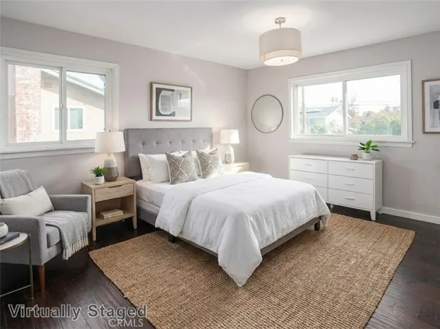 The primary suite is awash in natural light and offers sparkling windows, a modern light fixture, dual mirrored-door closets, and wood laminate floors. Virtually staged/enhanced photo