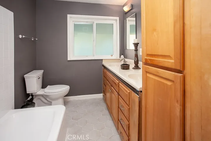 Guest bathroom with dual basin vanity, large dressing mirrors, tub and shower, and easy-care flooring.