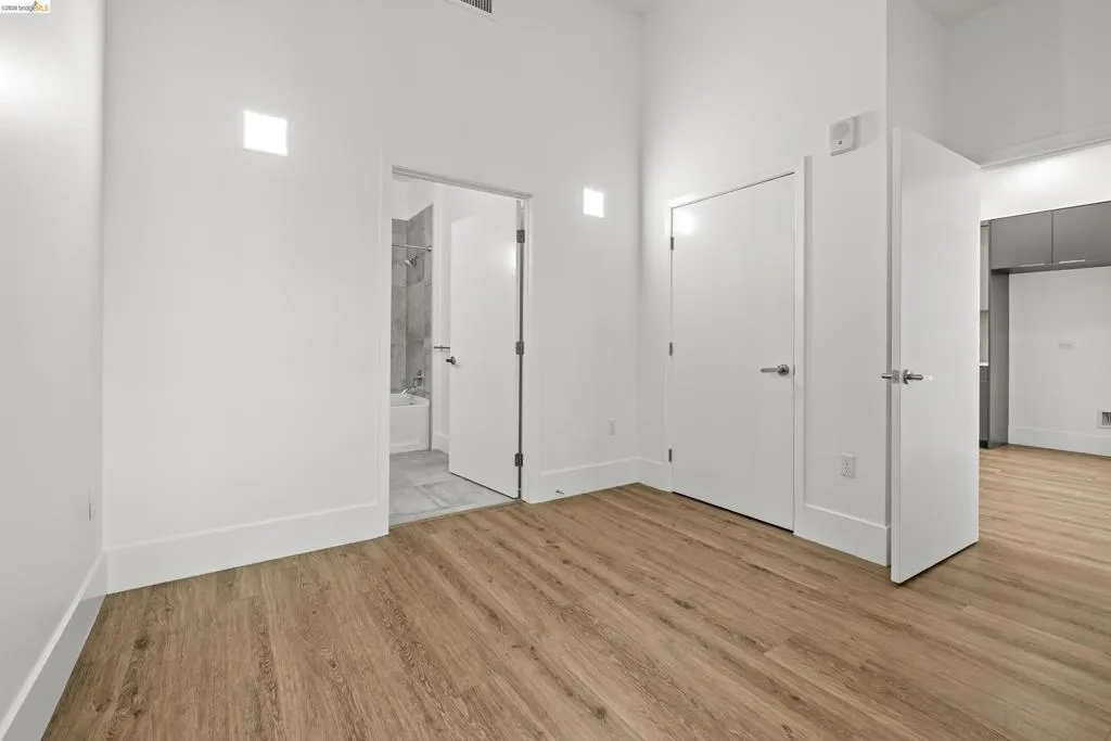 Unfurnished bedroom with light wood-style flooring, a towering ceiling, and connected bathroom