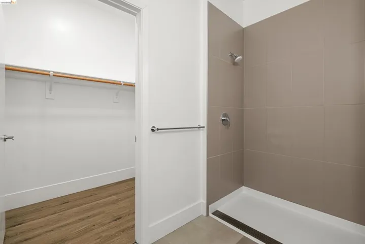 Full bath with a walk in closet, a stall shower, and light wood-style floors