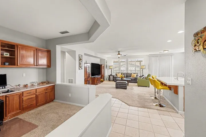 Kitchen featuring light carpet, a breakfast bar, light tile patterned floors, open shelves, and brown cabinetry