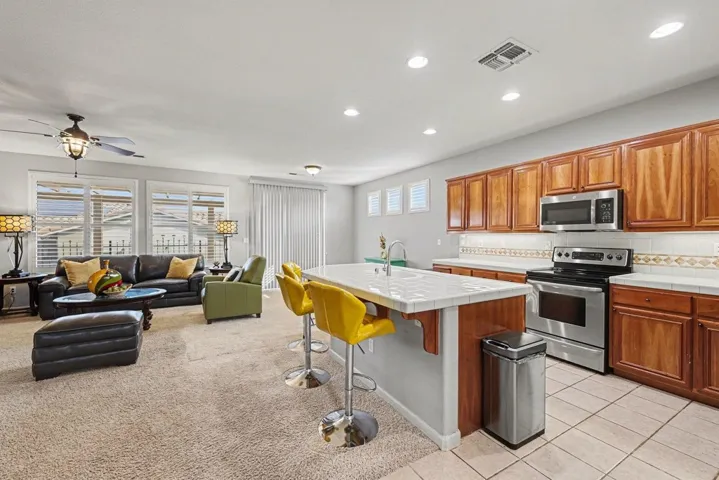 Kitchen featuring tile counters, appliances with stainless steel finishes, a breakfast bar, brown cabinetry, and recessed lighting