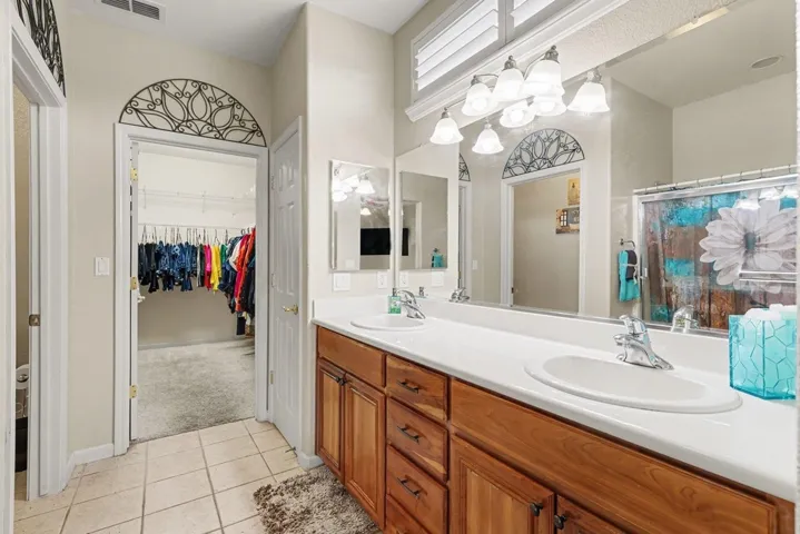 Bathroom with double vanity, a walk in closet, light tile patterned floors, and light colored carpet