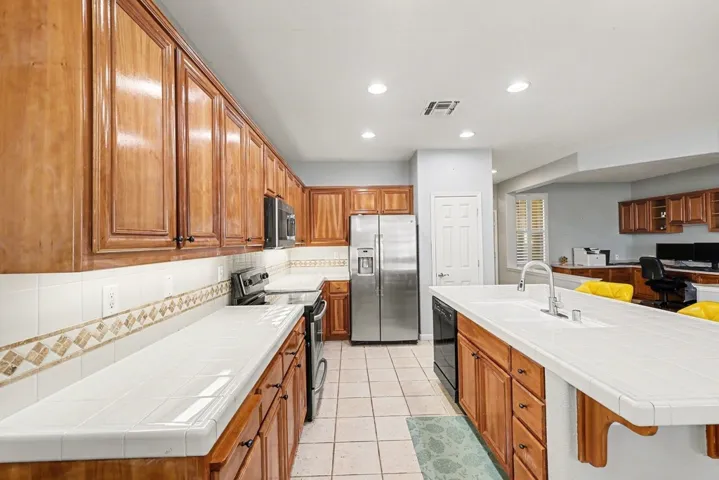 Kitchen with tile counters, brown cabinetry, appliances with stainless steel finishes, a breakfast bar, and recessed lighting