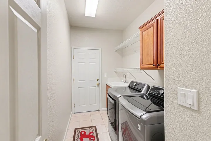 Laundry room featuring a textured wall, light tile patterned floors, washer and clothes dryer, and cabinet space