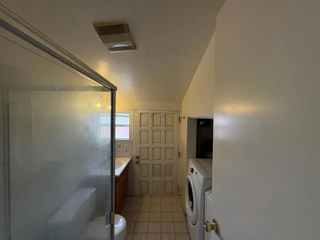 Bathroom featuring vanity, washer / dryer, light tile patterned floors, and a shower with door