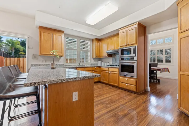 Kitchen featuring a peninsula, a breakfast bar area, appliances with stainless steel finishes, dark wood-style floors, and light stone countertops