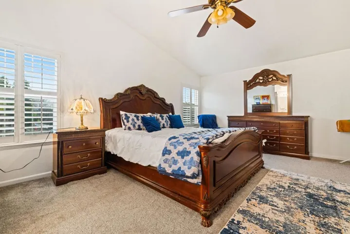 Bedroom with light carpet, a ceiling fan, and vaulted ceiling
