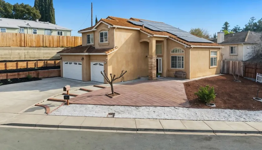 Traditional-style house featuring roof mounted solar panels, stucco siding, concrete driveway, and an attached garage
