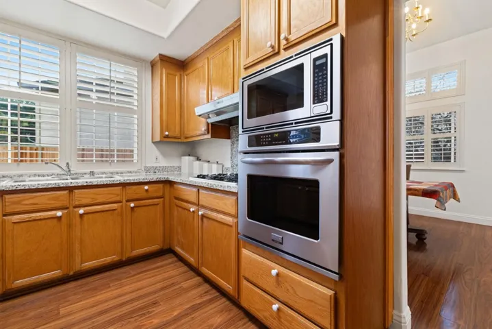 Kitchen with dark wood-style floors, stainless steel appliances, brown cabinets, under cabinet range hood, and a chandelier