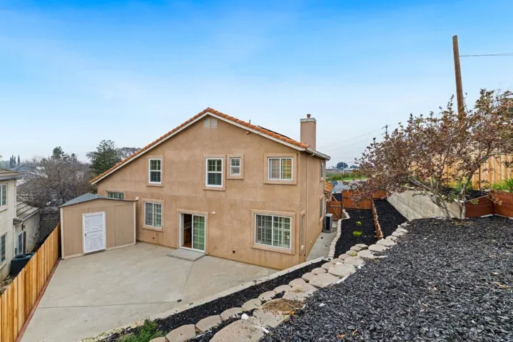 Rear view of house featuring a storage shed, a fenced backyard, a patio, a chimney, and stucco siding