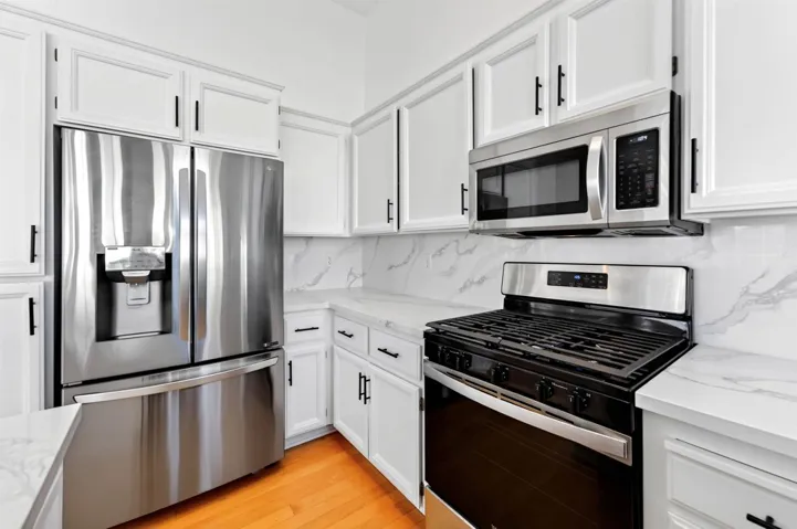 Kitchen with stainless steel appliances, white cabinetry, light stone countertops, light wood-type flooring, and tasteful backsplash