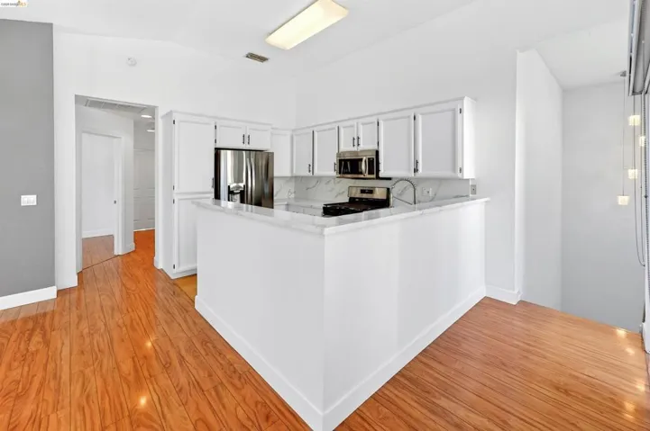 Kitchen featuring a peninsula, white cabinets, stainless steel appliances, light stone counters, and vaulted ceiling
