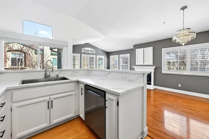 Kitchen featuring white cabinetry, stainless steel dishwasher, light wood-style flooring, vaulted ceiling, and a chandelier