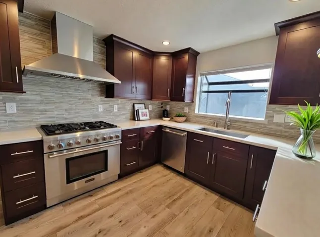 Kitchen featuring wall chimney range hood, appliances with stainless steel finishes, light wood finished floors, dark brown cabinetry, and recessed lighting