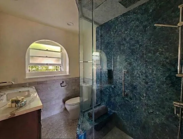 Full bathroom featuring vanity, tile walls, a marble finish shower, wainscoting, and tile patterned floors