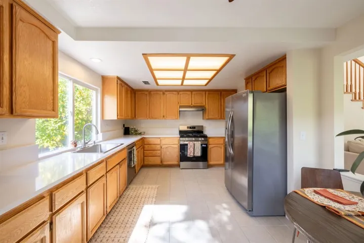 Kitchen featuring stainless steel appliances, light countertops, brown cabinetry, light tile patterned floors, and recessed lighting