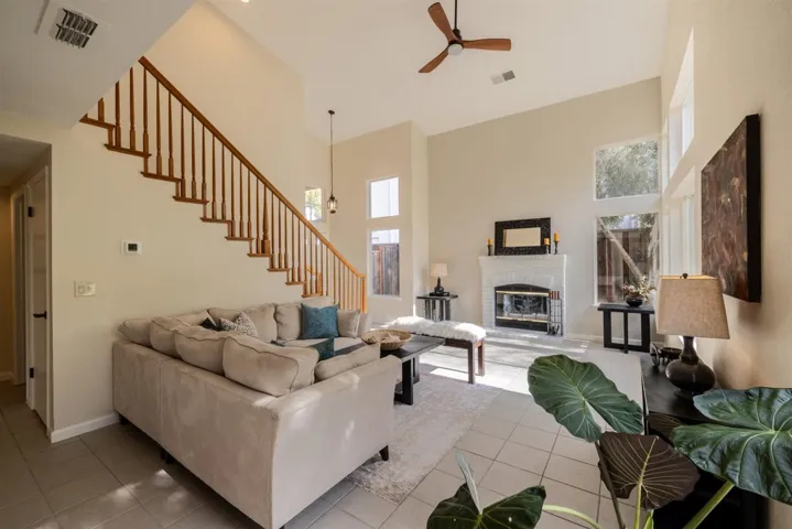 Living area featuring light tile patterned floors, a towering ceiling, healthy amount of natural light, a fireplace, and ceiling fan