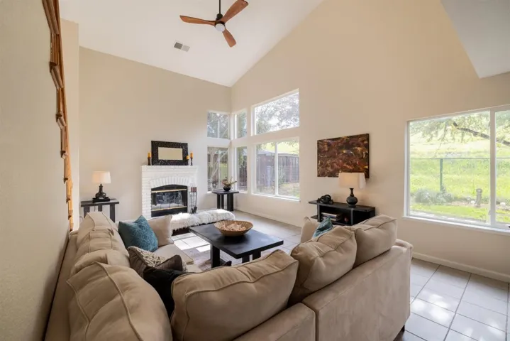 Living room with light tile patterned floors, high vaulted ceiling, a ceiling fan, and a fireplace