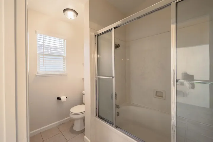 Bathroom featuring enclosed tub / shower combo and light tile patterned flooring