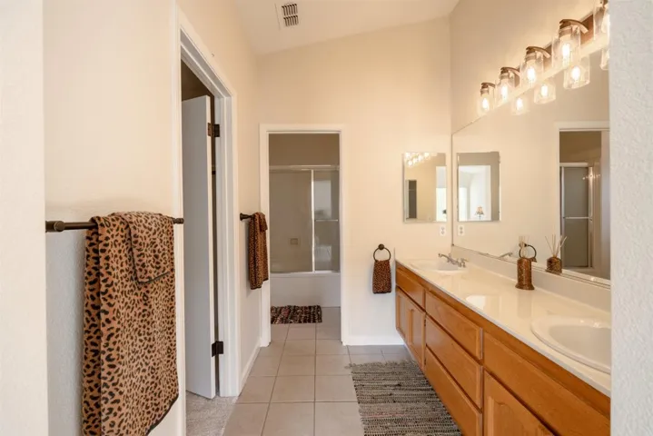 Full bathroom with double vanity, light tile patterned floors, and enclosed tub / shower combo