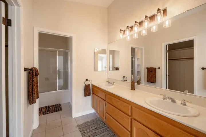 Full bath with shower / bath combination with glass door, double vanity, light tile patterned floors, and a spacious closet