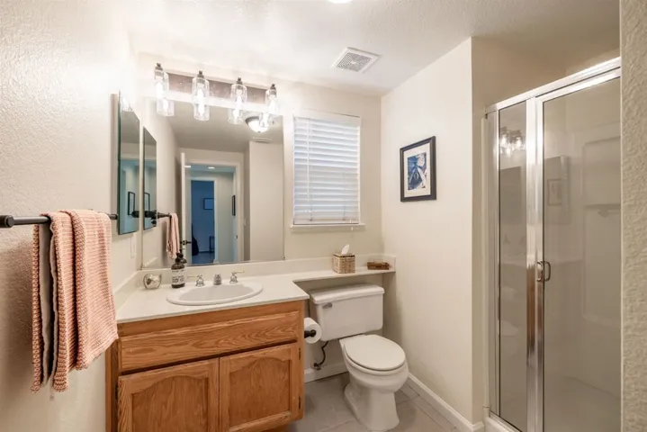 Bathroom with a shower stall, vanity, light tile patterned floors, and a textured ceiling