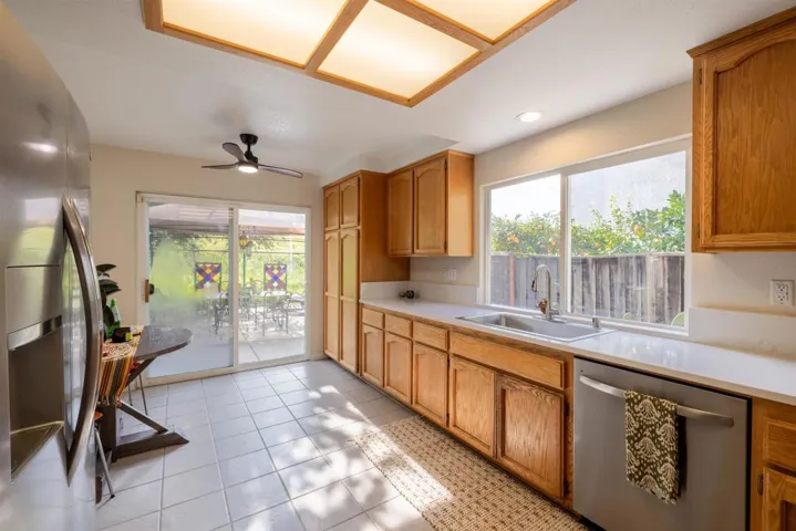 Kitchen with appliances with stainless steel finishes, light countertops, light tile patterned floors, a ceiling fan, and brown cabinetry