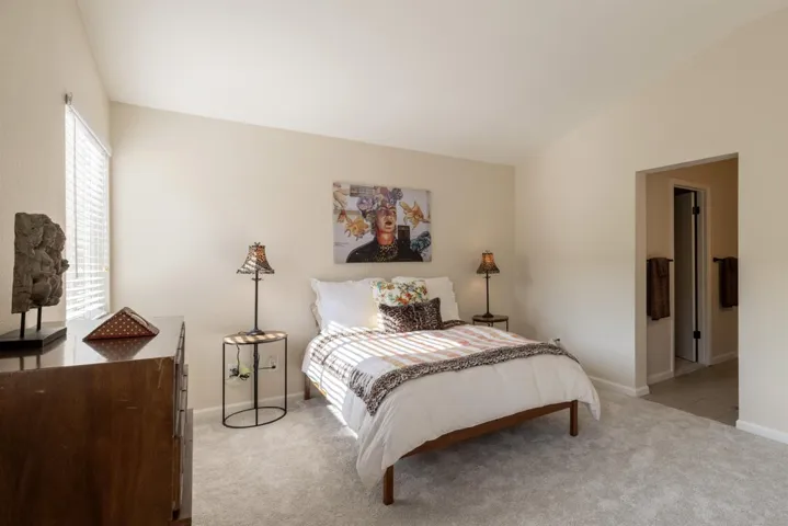 Bedroom featuring light colored carpet, lofted ceiling, and ensuite bath