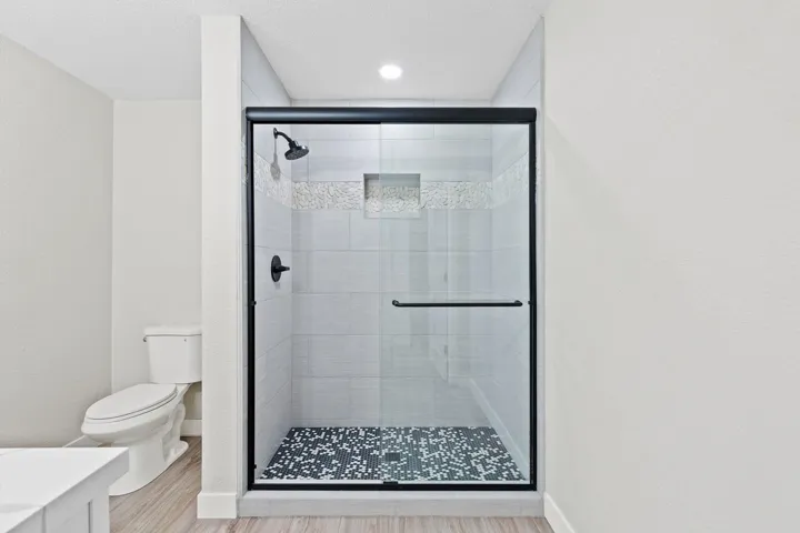 Full bathroom featuring a shower stall, light wood-style floors, a textured ceiling, and a textured wall