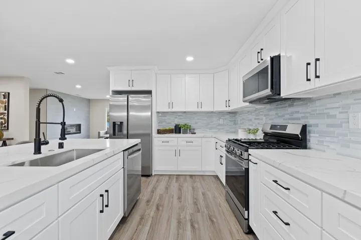 Kitchen featuring stainless steel appliances, white cabinetry, light stone counters, light wood-style floors, and recessed lighting