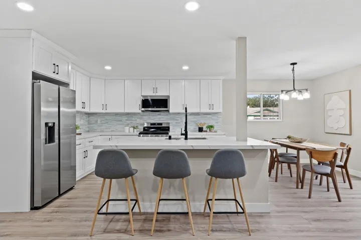 Kitchen featuring white cabinets, appliances with stainless steel finishes, decorative light fixtures, light stone countertops, and recessed lighting
