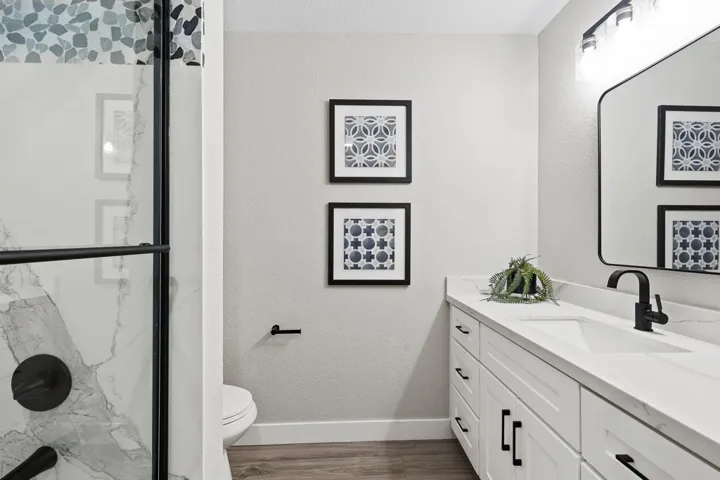 Full bathroom featuring vanity, a textured wall, a marble finish shower, and dark wood-style flooring