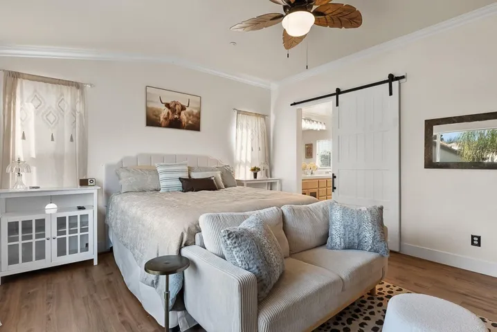 Bedroom featuring a barn door, ensuite bath, wood finished floors, a ceiling fan, and crown molding