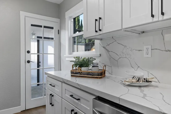 Kitchen featuring white cabinetry, light stone counters, dishwasher, light wood finished floors, and a textured wall
