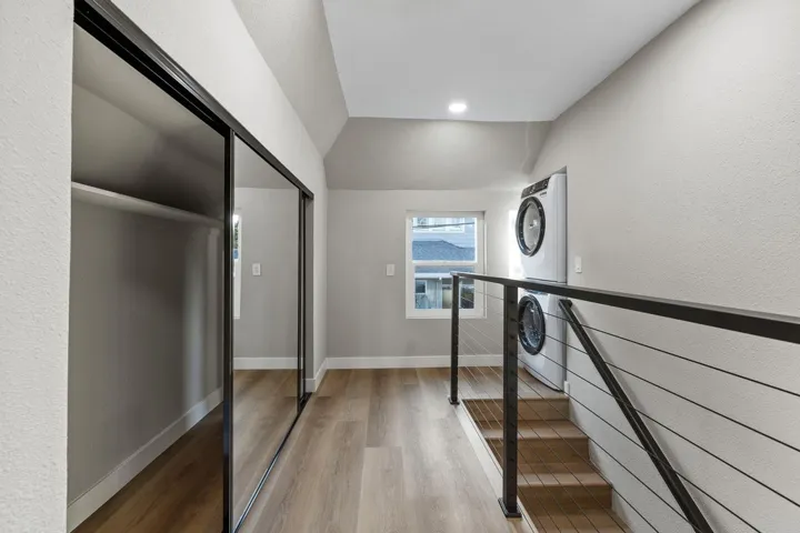 Hall with light wood finished floors, lofted ceiling, estacked washer and dryer, a textured wall, and recessed lighting