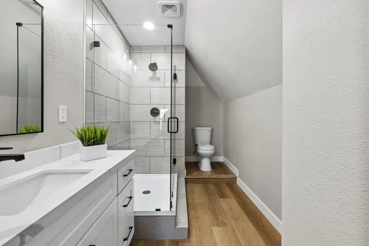 Full bath with a textured wall, vanity, a stall shower, light wood finished floors, and vaulted ceiling