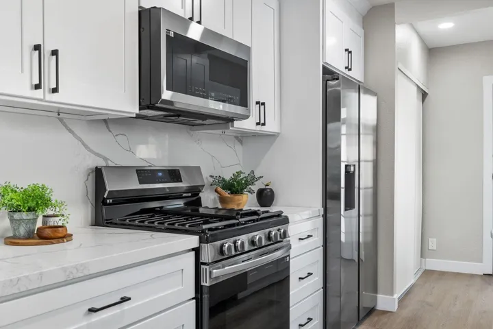 Kitchen featuring appliances with stainless steel finishes, white cabinetry, light stone countertops, decorative backsplash, and light wood-type flooring