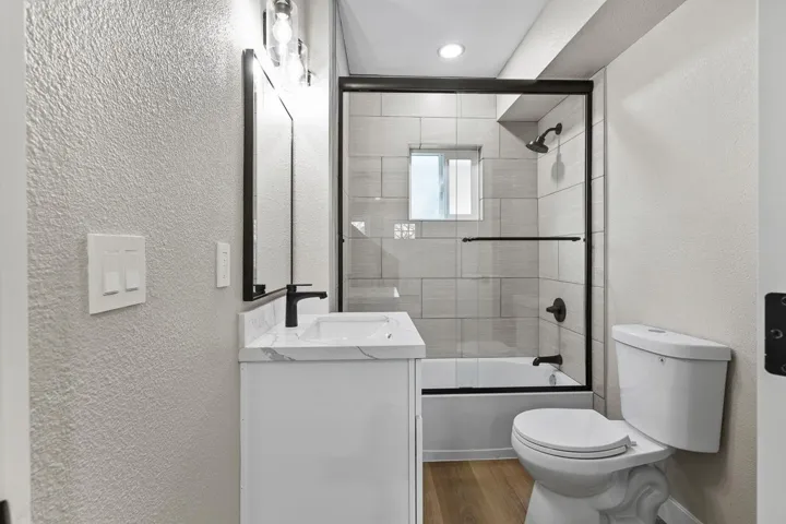 Full bath featuring a textured wall, enclosed tub / shower combo, vanity, and wood finished floors