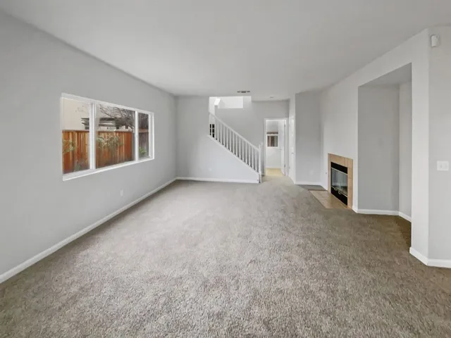 Unfurnished living room with a tiled fireplace, carpet floors, and stairway