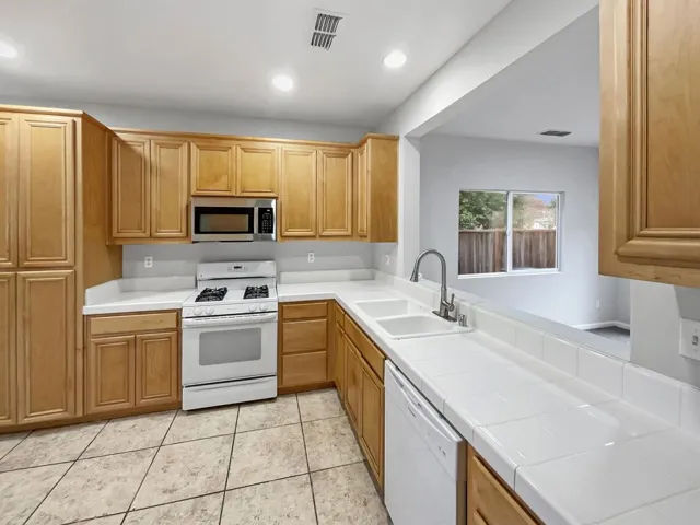 Kitchen with tile countertops, white appliances, recessed lighting, and light tile patterned floors