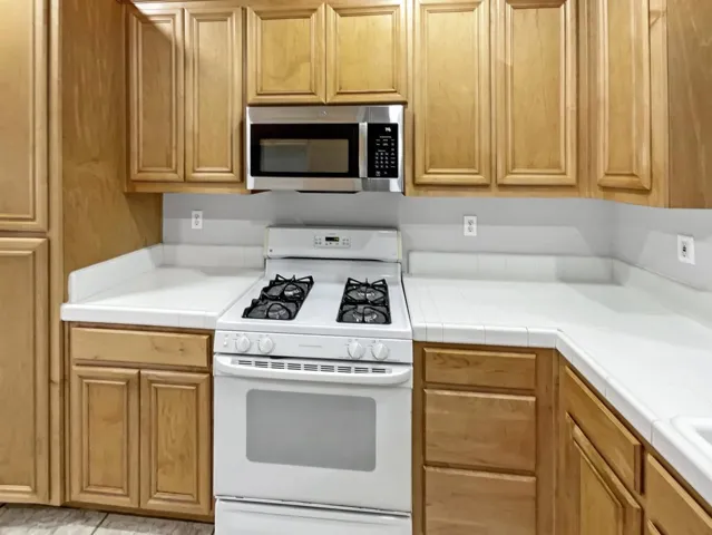 Kitchen with tile counters, white range with gas stovetop, and stainless steel microwave