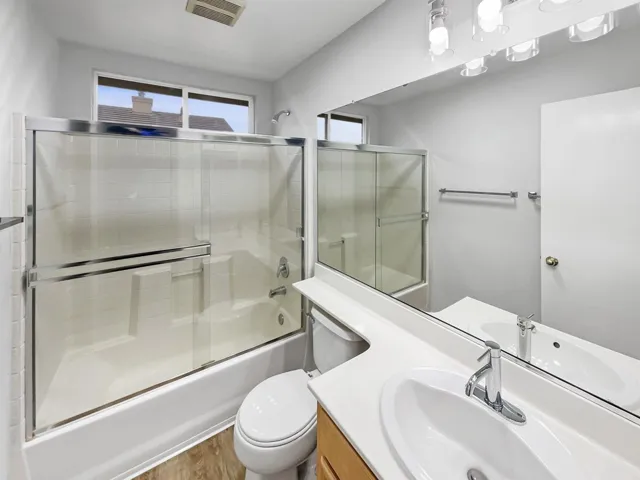 Bathroom with vanity, bath / shower combo with glass door, and healthy amount of natural light